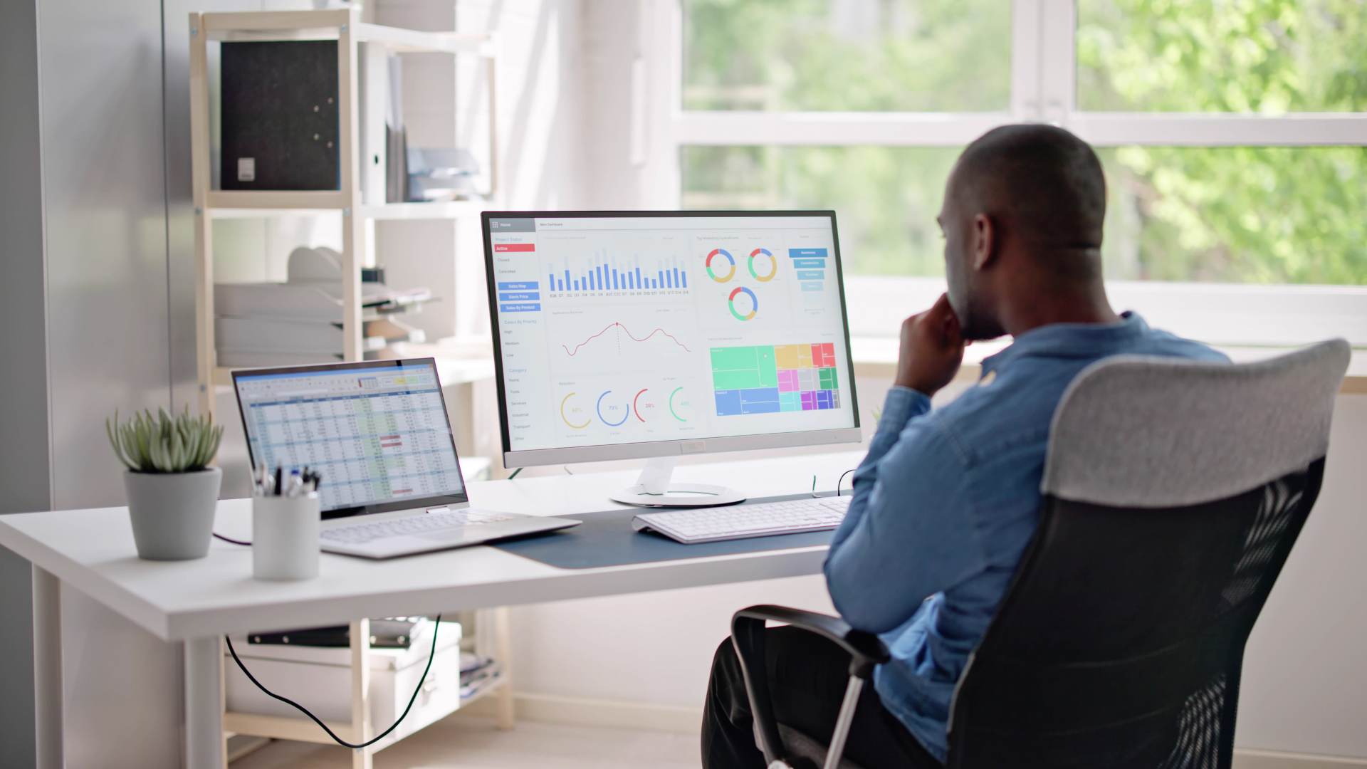 Man at desk analyzing charts on computer and laptop.