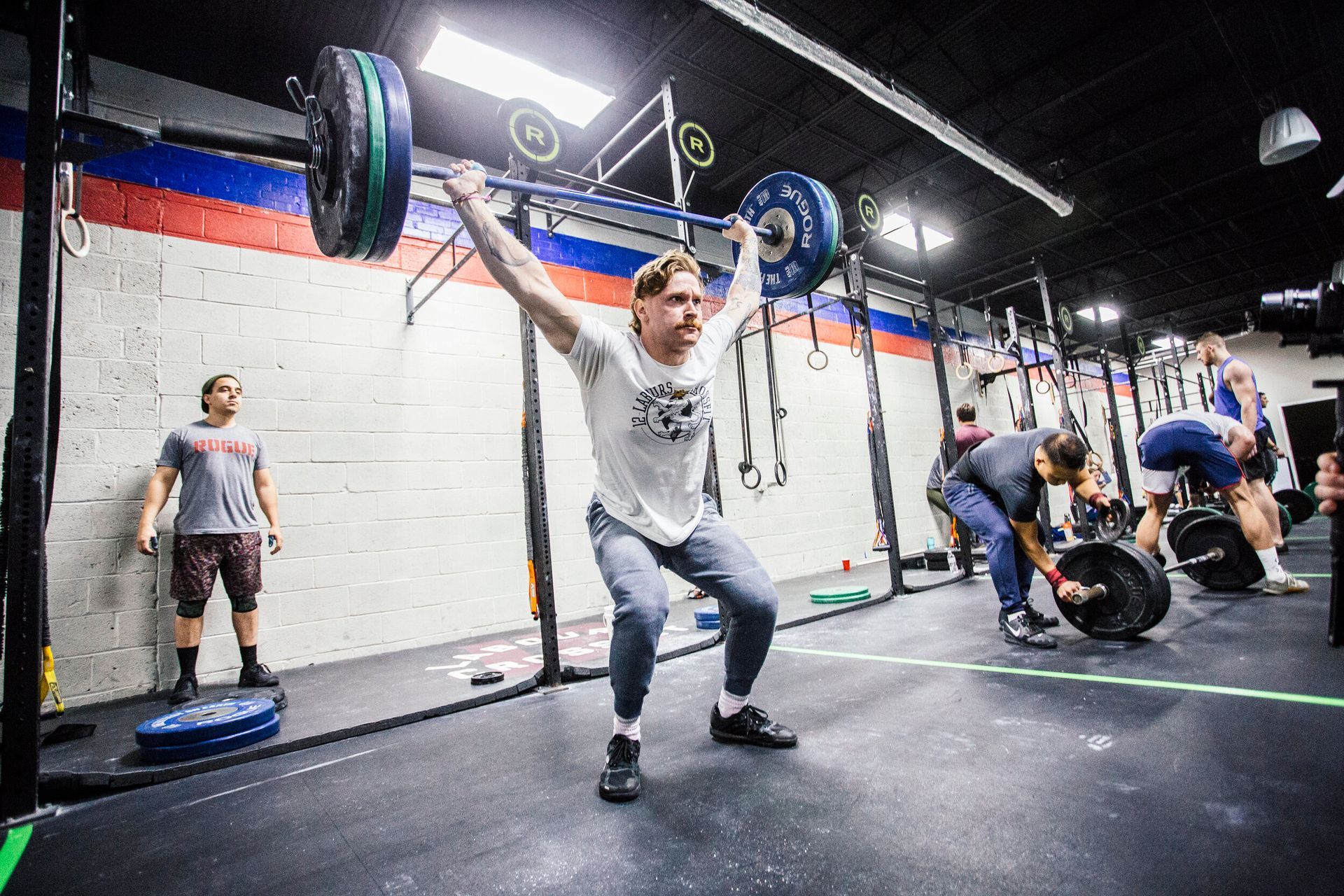 A man is squatting with a barbell over his head in a gym.