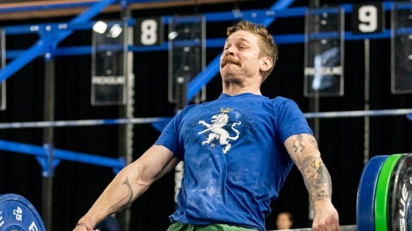 A man in a blue shirt is lifting a barbell in a gym.