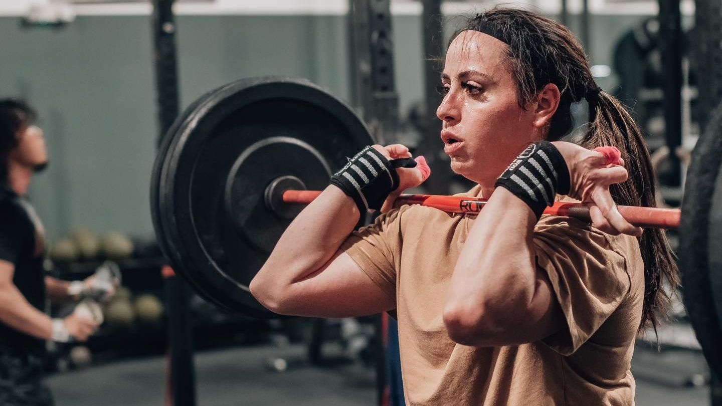 A woman is lifting a barbell over her head in a gym.