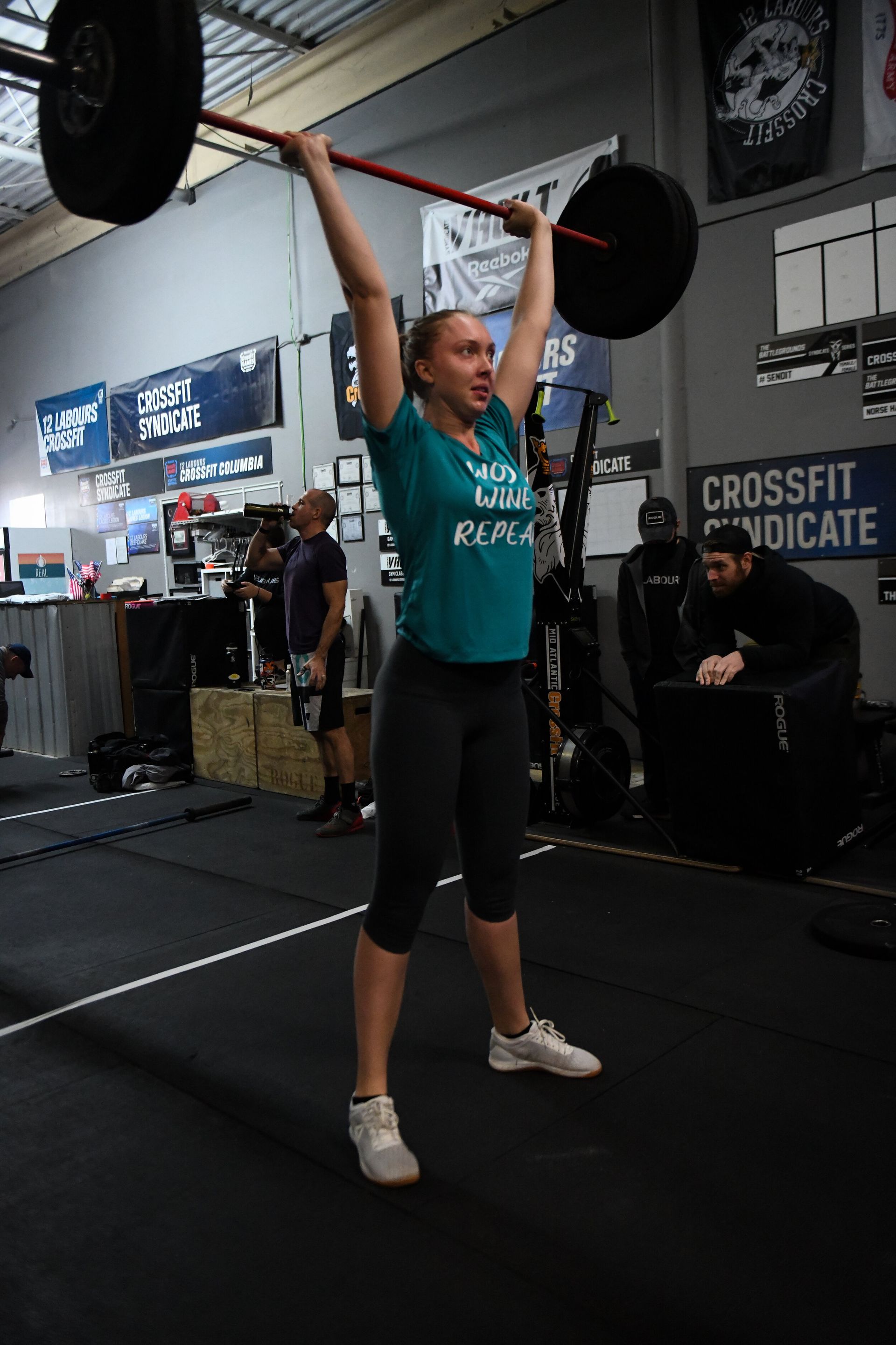 A woman is lifting a barbell over her head in a gym.