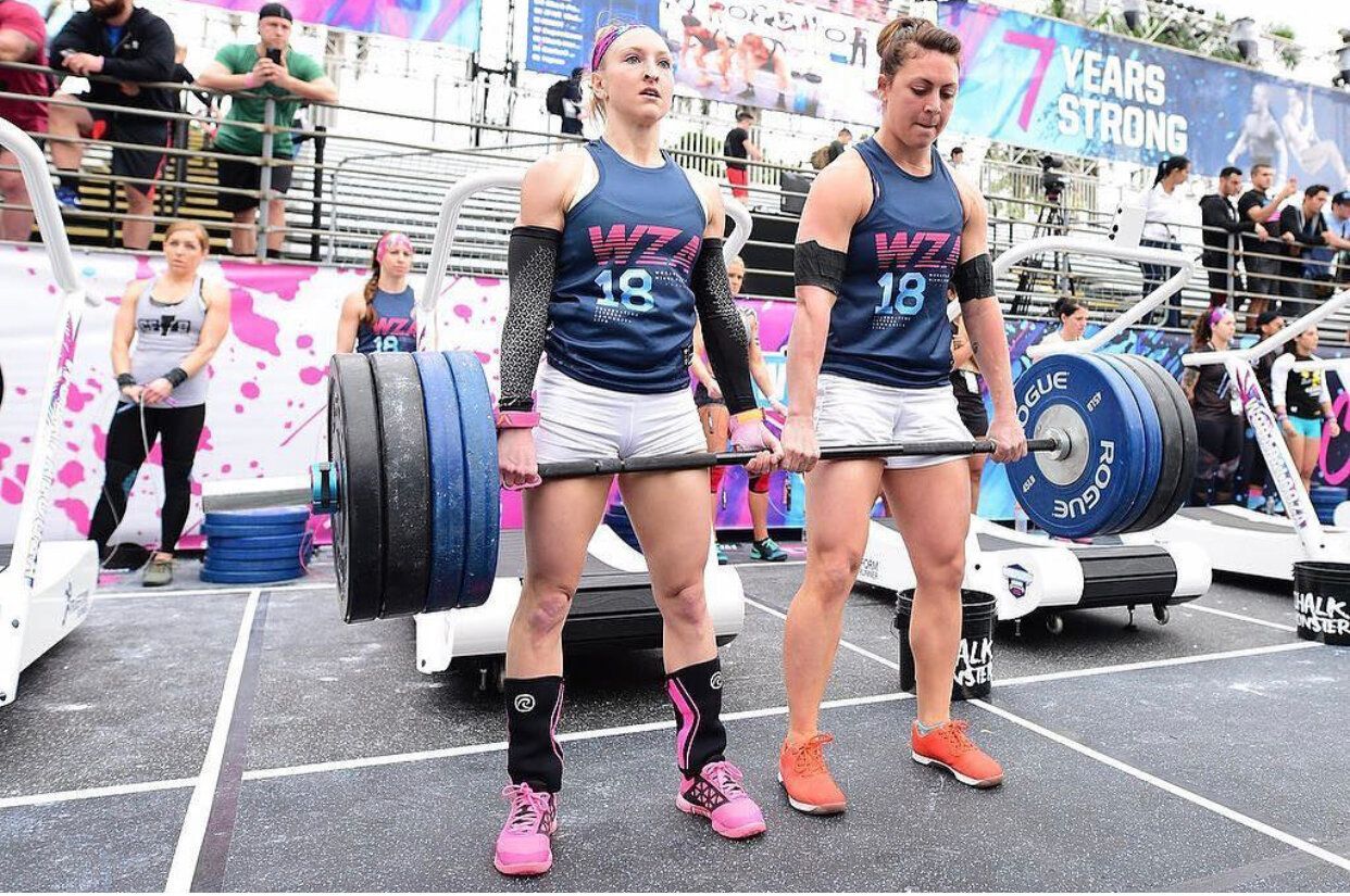 Two women are lifting a barbell in a gym.