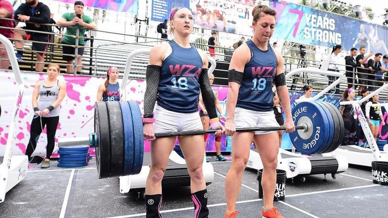 Two women are lifting a barbell in a gym.