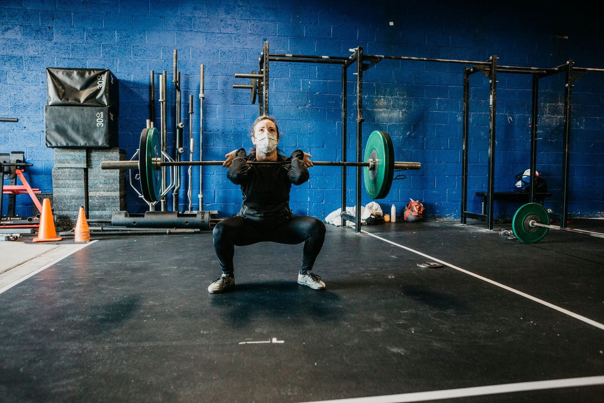 A man is squatting with a barbell over his head in a gym.