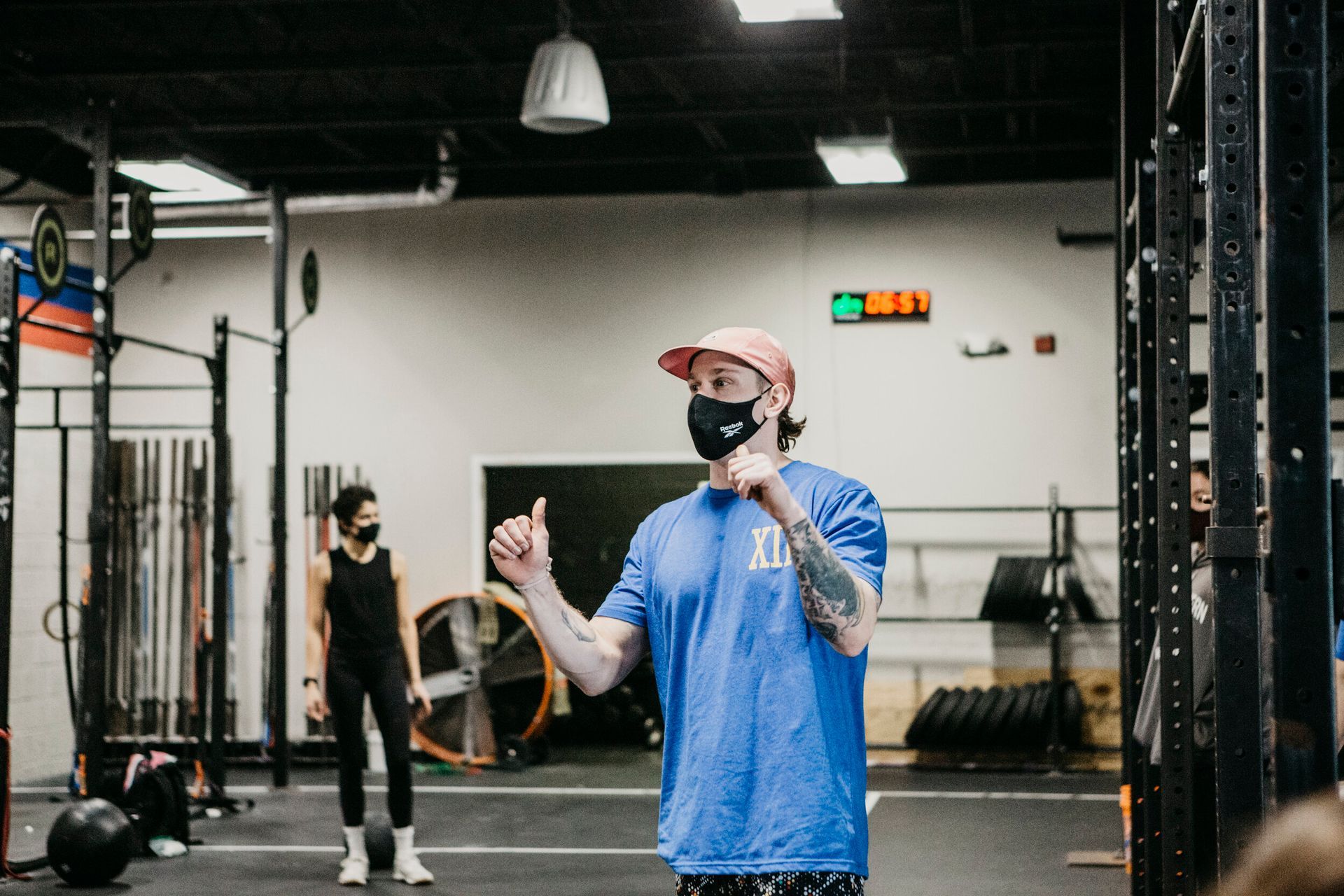 A man wearing a mask is giving a thumbs up in a gym.