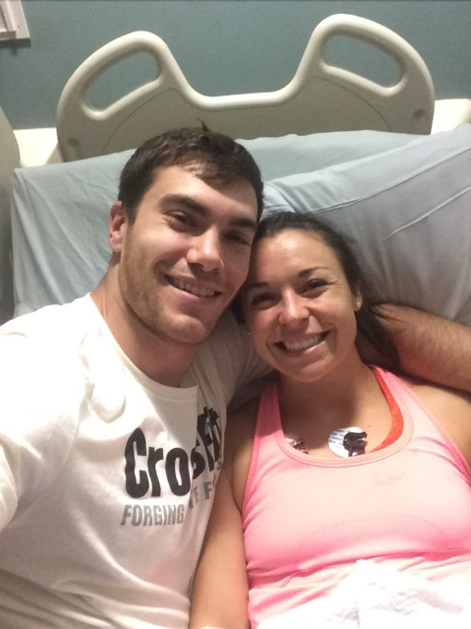 A man wearing a crossfit shirt is laying next to a woman in a hospital bed