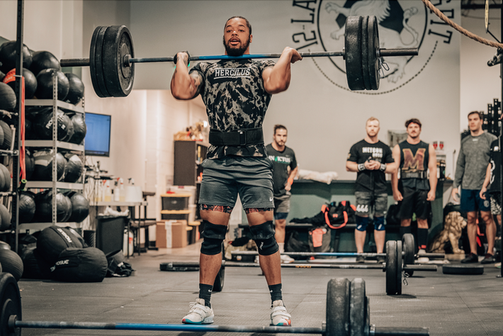 A man is lifting a barbell over his head in a gym.