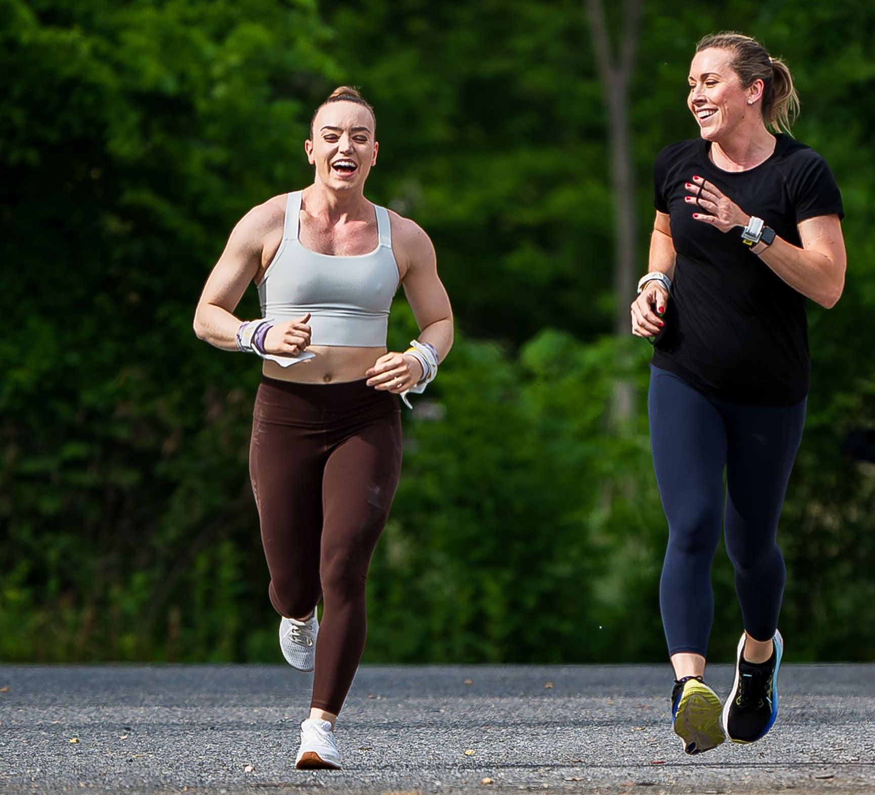 Two women are running down a road together and smiling.