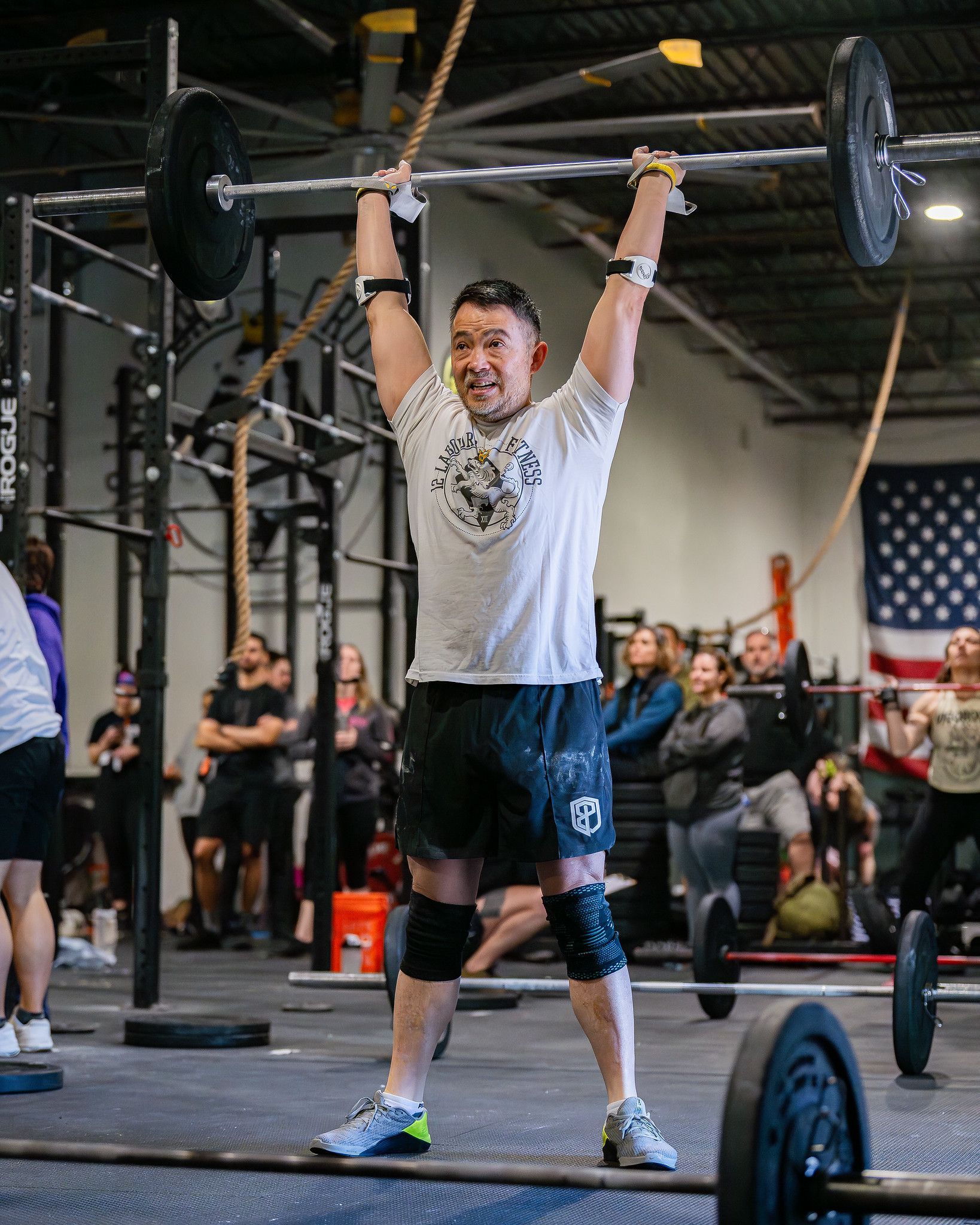 A man is lifting a barbell over his head in a gym.