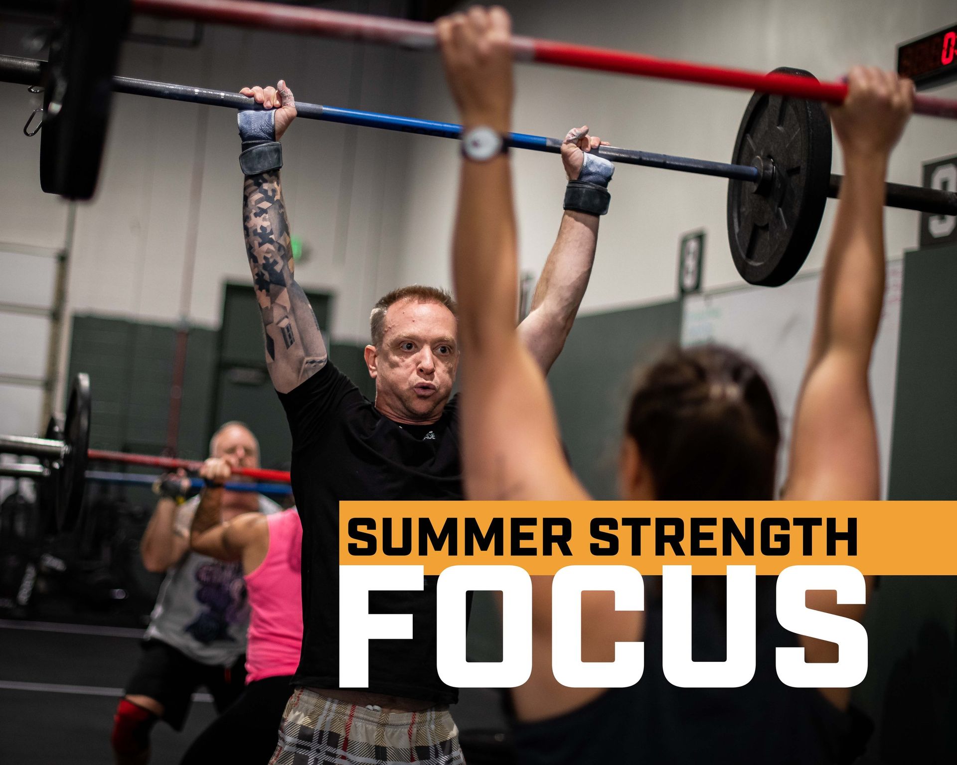 A man is lifting a barbell over his head in a gym.