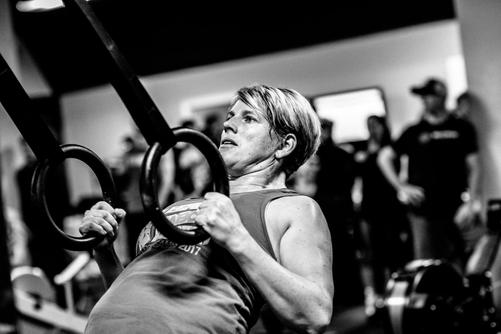 A black and white photo of a woman using gymnastic rings in a gym.