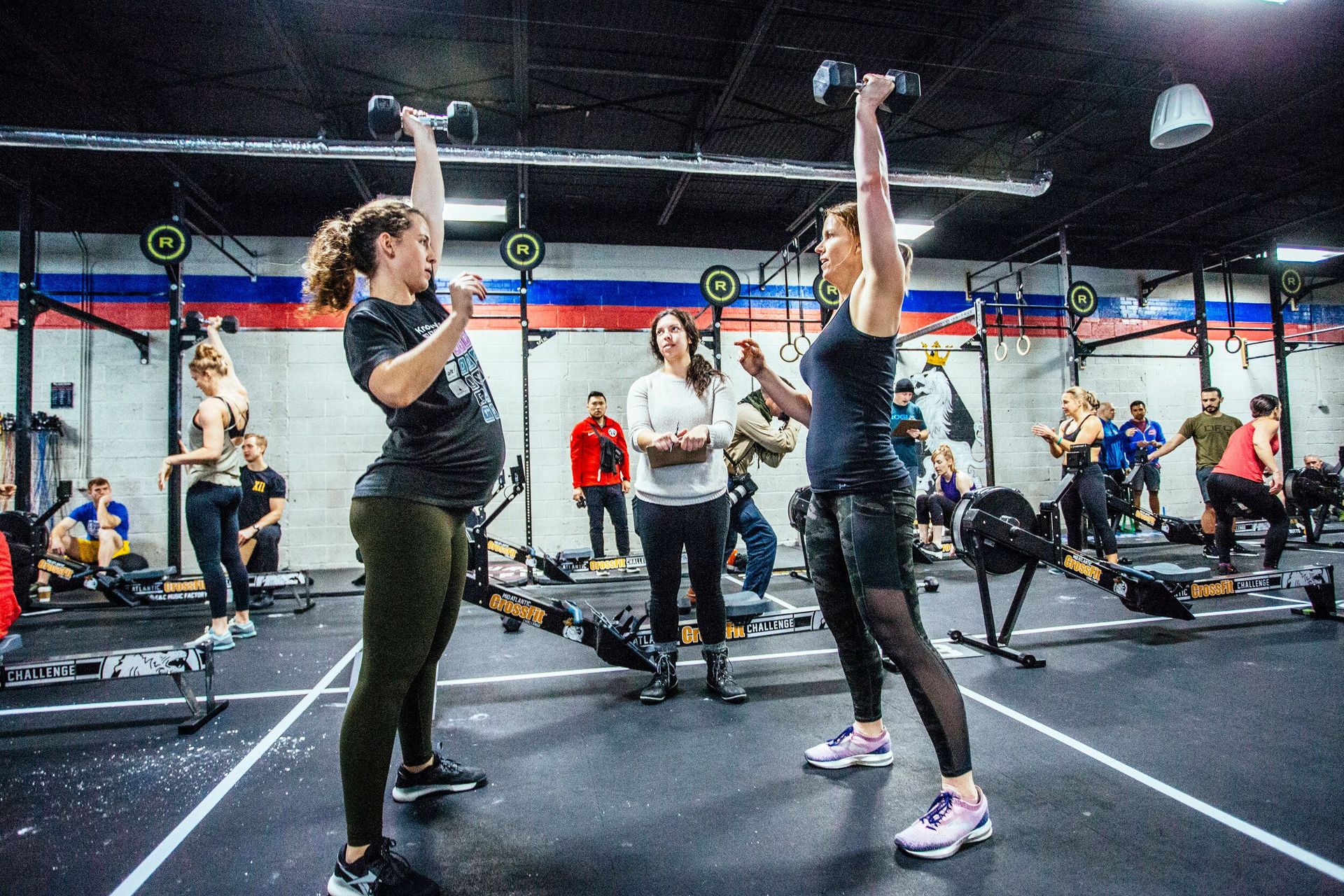 Two women are lifting dumbbells in a gym.