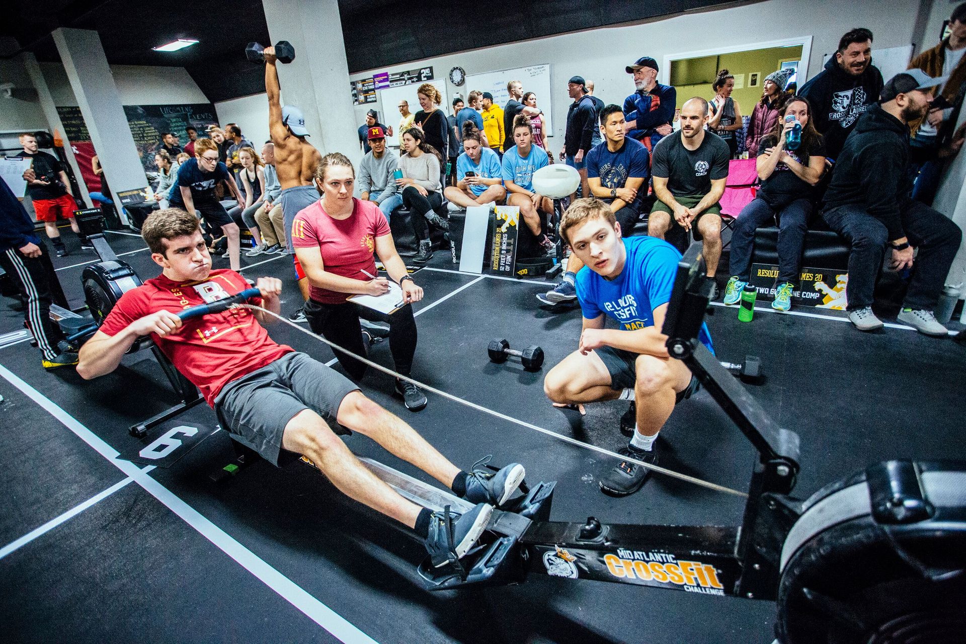 A group of people are sitting around a rowing machine in a gym.