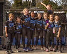 Baseball glove with ball on green grass, with blurred baseballs in the background.