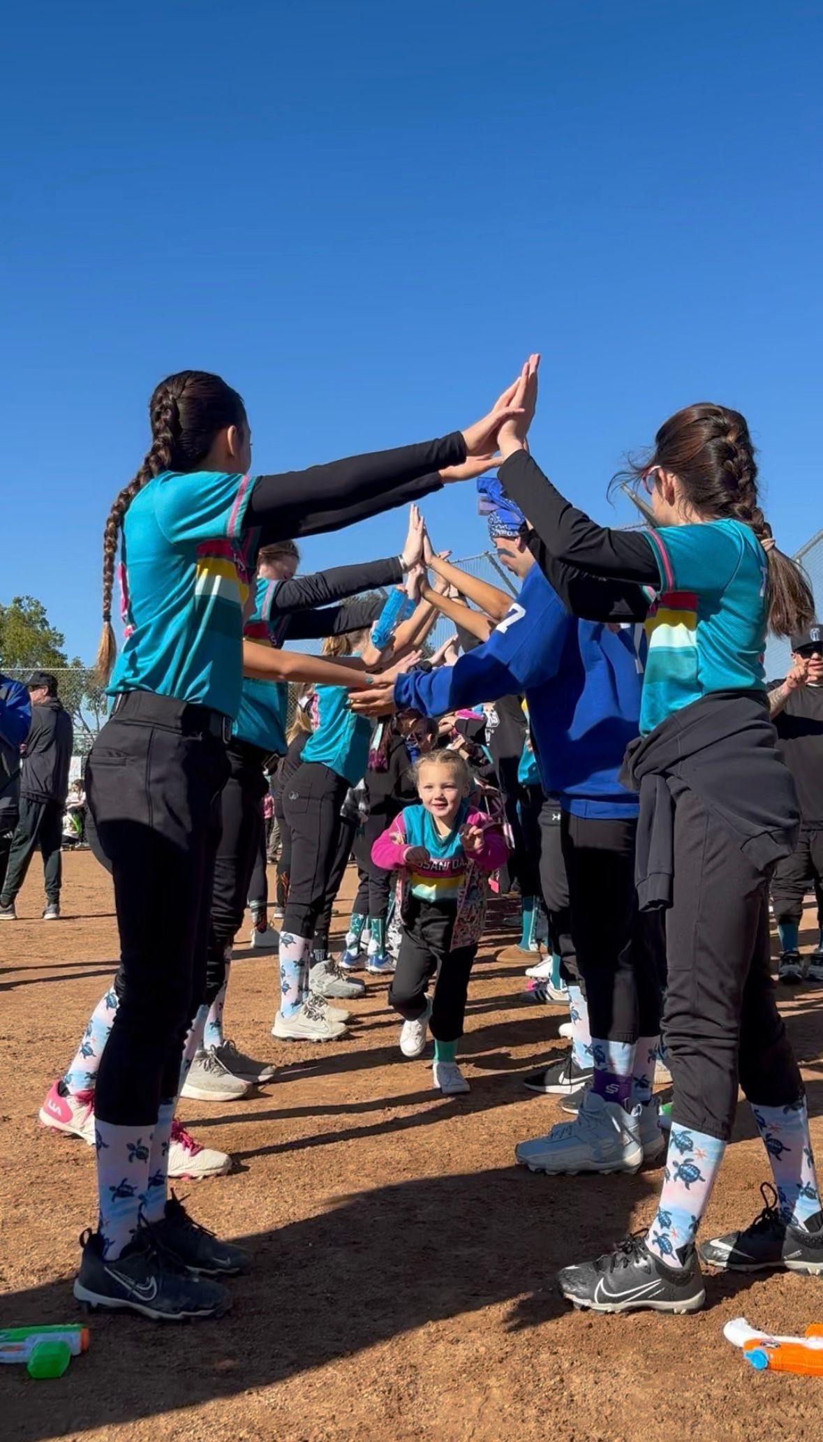 A person wearing a hat and orange shirt, holding a baseball bat on their shoulder on a baseball field.