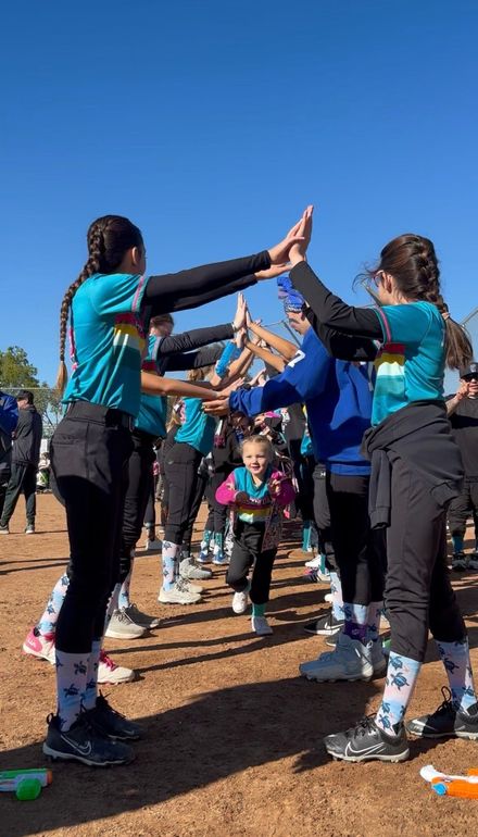 A person wearing a hat and orange shirt, holding a baseball bat on their shoulder on a baseball field.