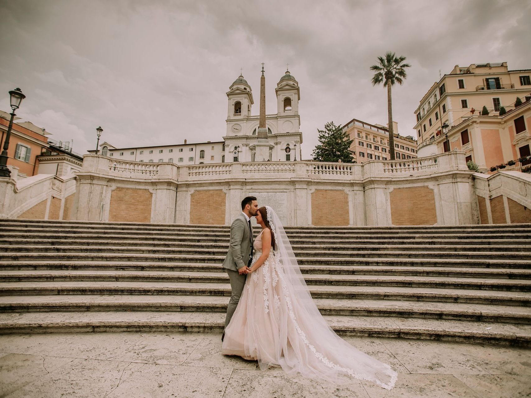 A bride and groom are kissing on the steps of a building.