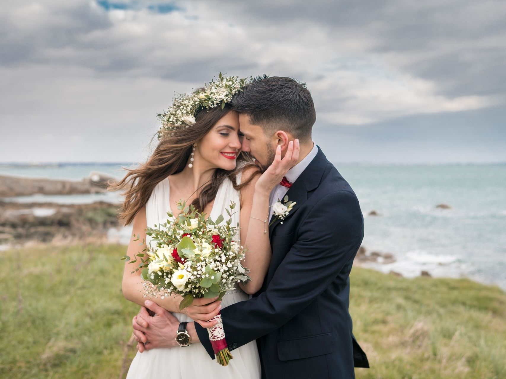 A bride and groom are posing for a picture in front of the ocean.
