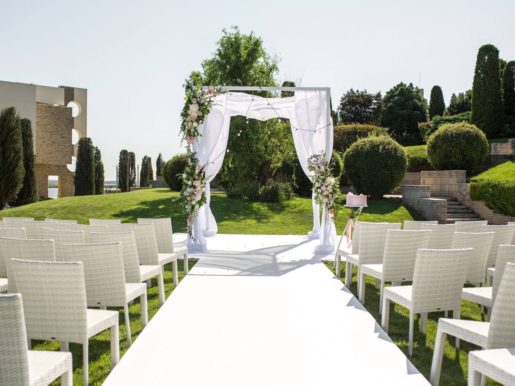 A row of white chairs are lined up in front of a wedding arch.