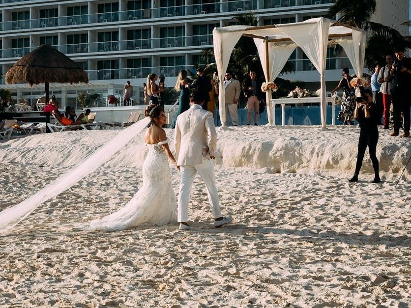 A bride and groom are walking on the beach holding hands.