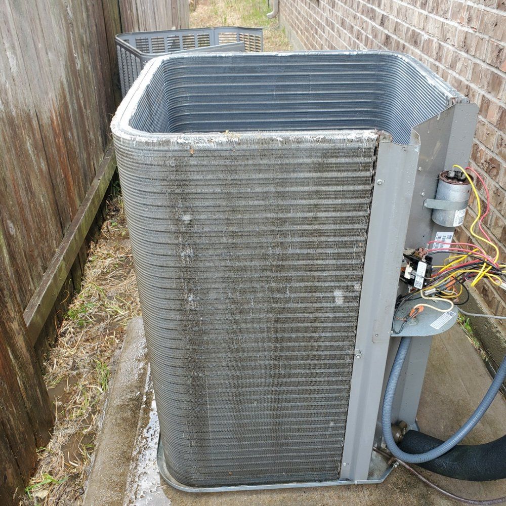 A dirty air conditioner is sitting on a sidewalk next to a brick wall.