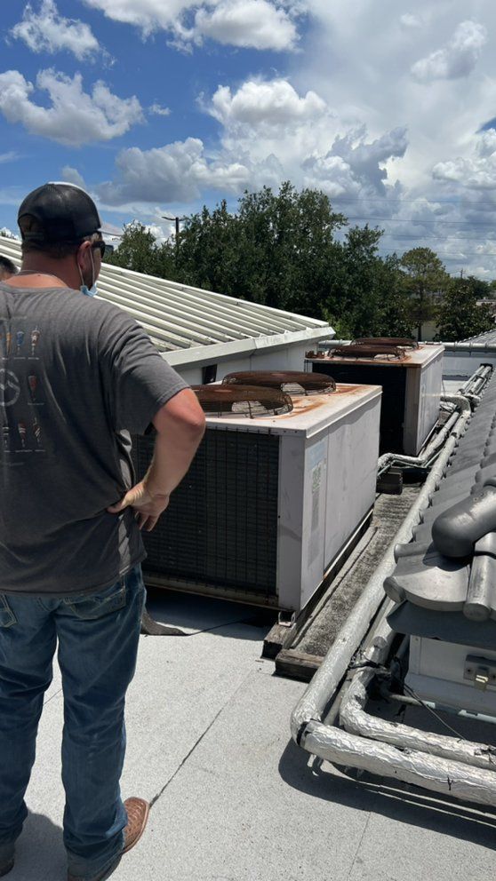 A man is standing on the roof of a building looking at the air conditioners.