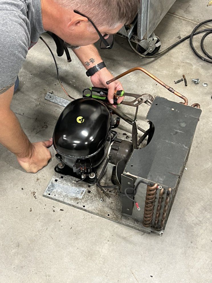 A man is working on a refrigerator compressor.
