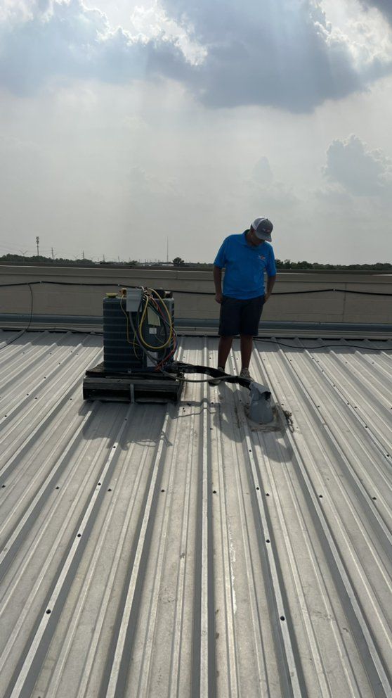 A man is standing on top of a metal roof with a vacuum cleaner.