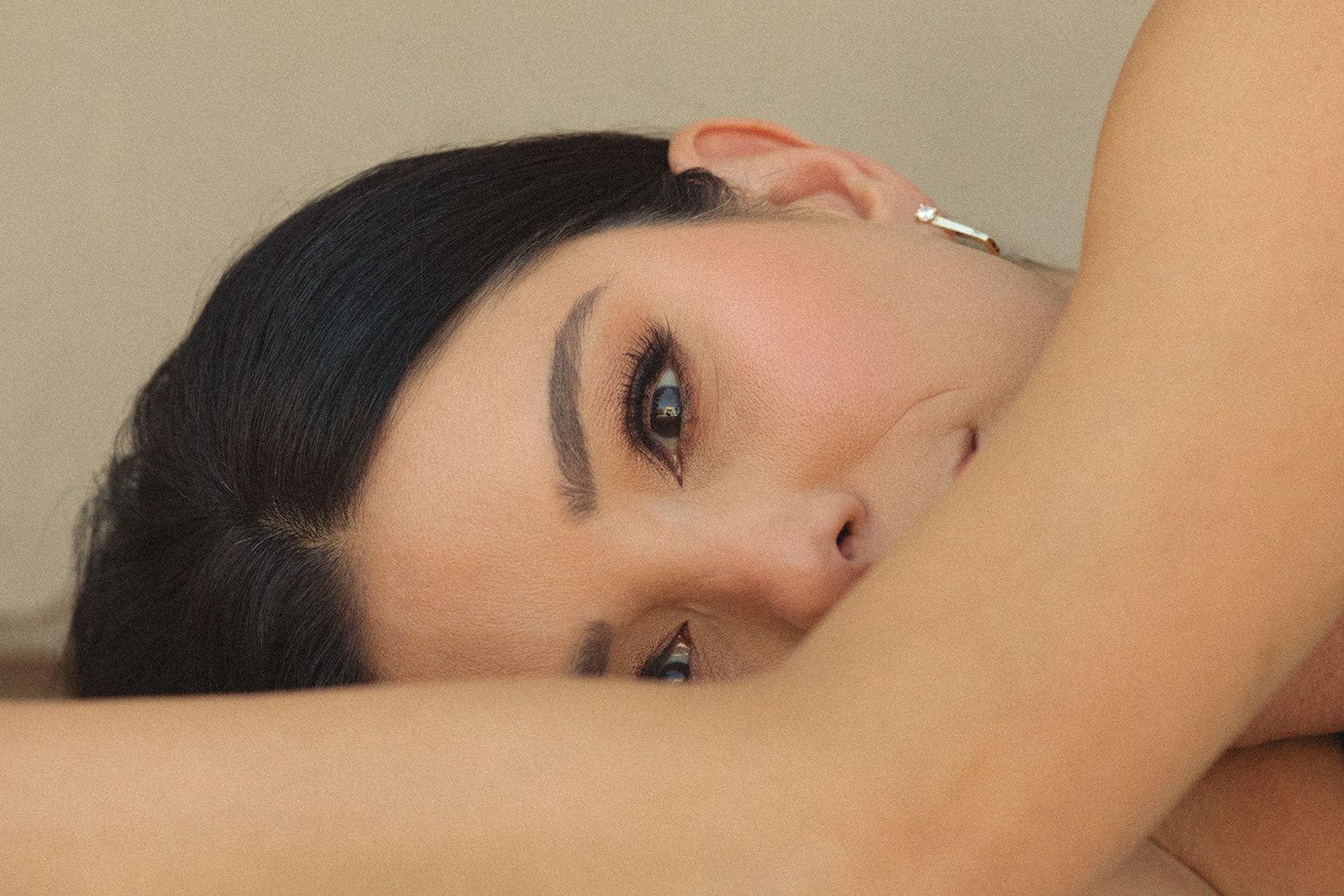 Close-up of a person resting their face on a bare arm, looking towards the camera with a neutral expression.