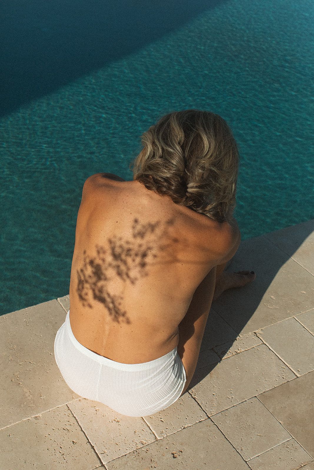 a woman sitting with her back to the camera near a pool