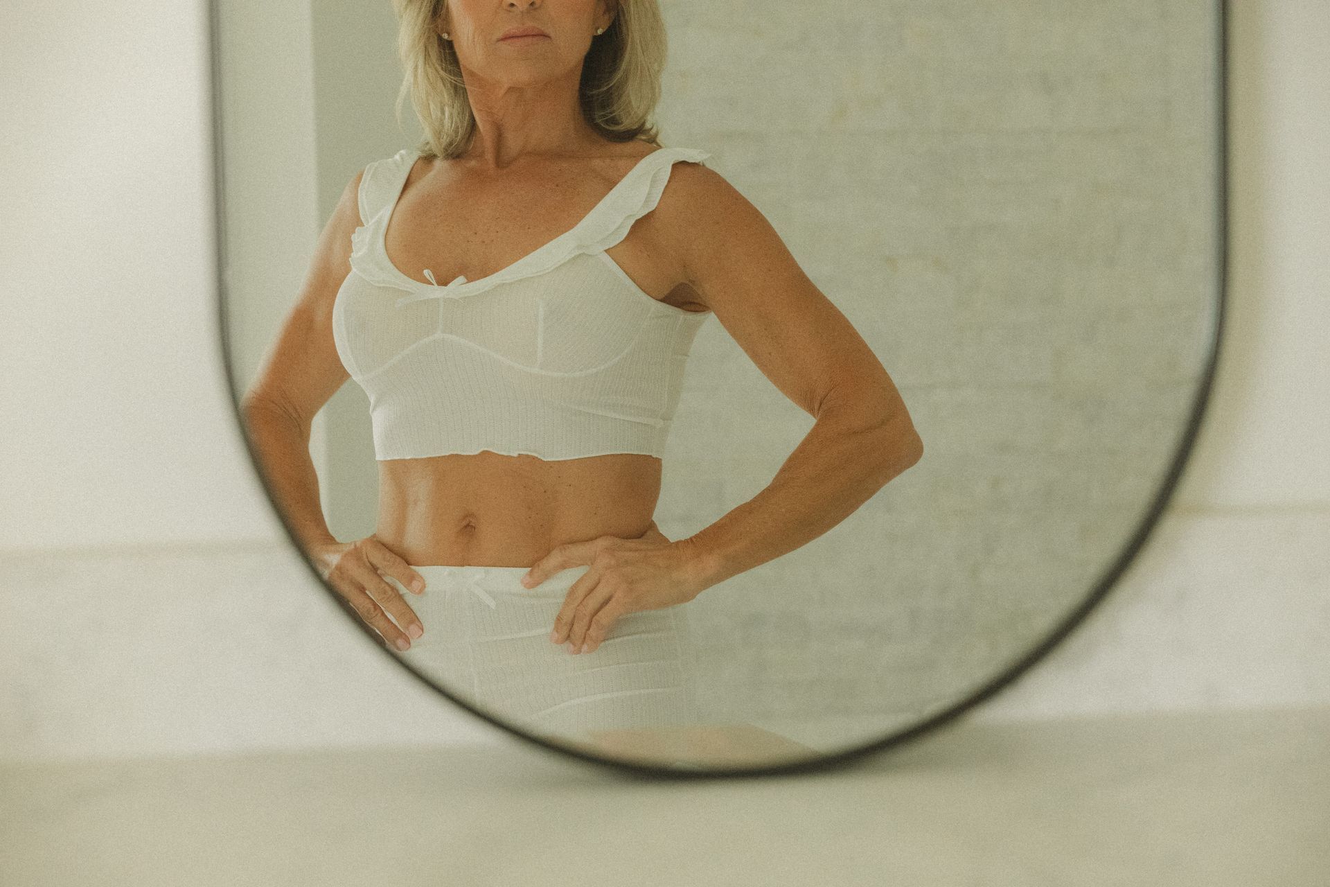A woman is standing in front of a round mirror.