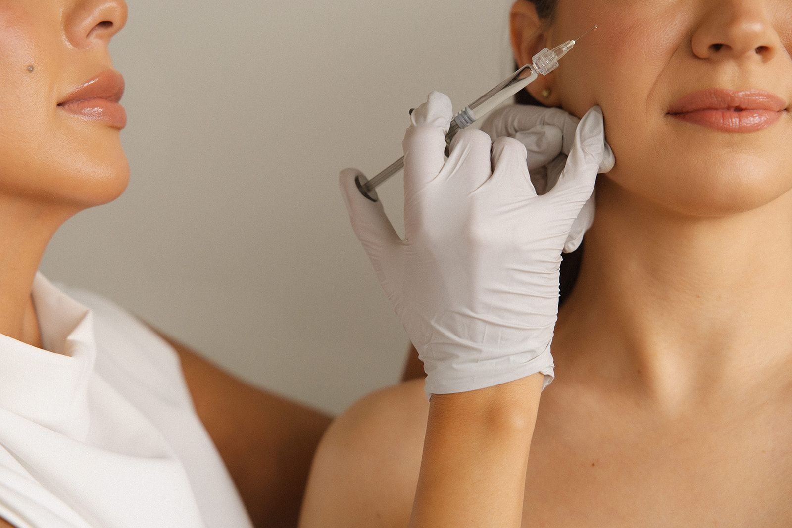 A practitioner in gloves uses a syringe to perform a cosmetic facial injection on a person's cheek.