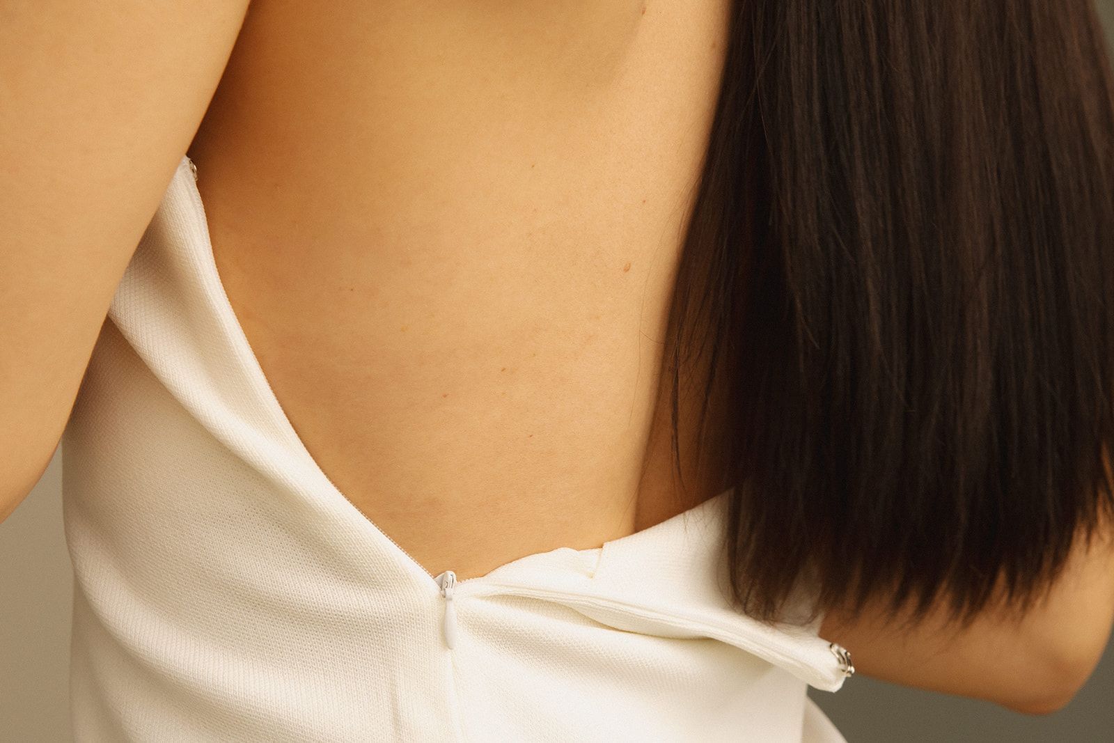 A close-up view of the back of a person wearing a white sleeveless garment with a partially unzipped zipper.