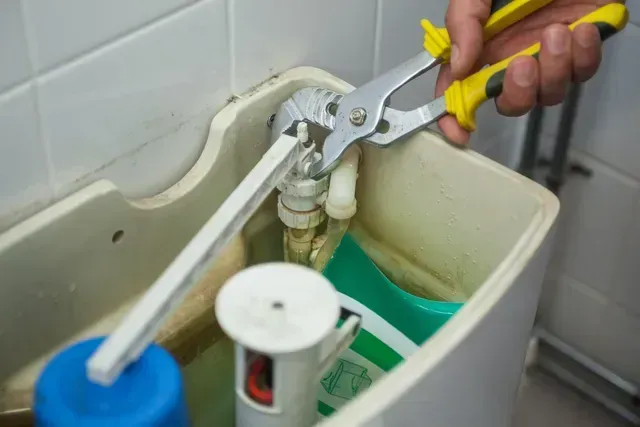 Hand using pliers to adjust a toilet tank valve, with water inside the tank