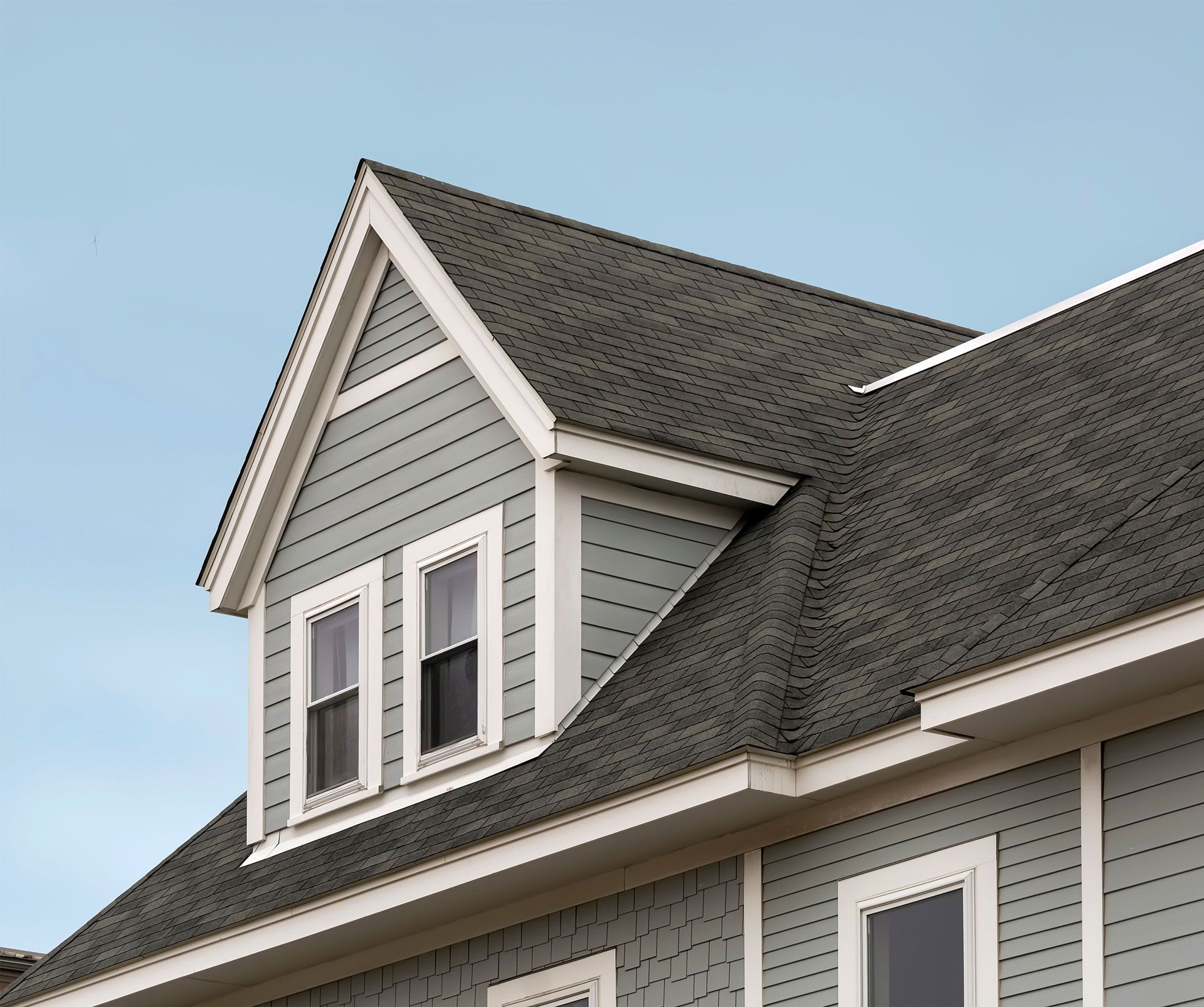 Gray house roof with dormer, two windows, blue siding, and dark gray shingles.