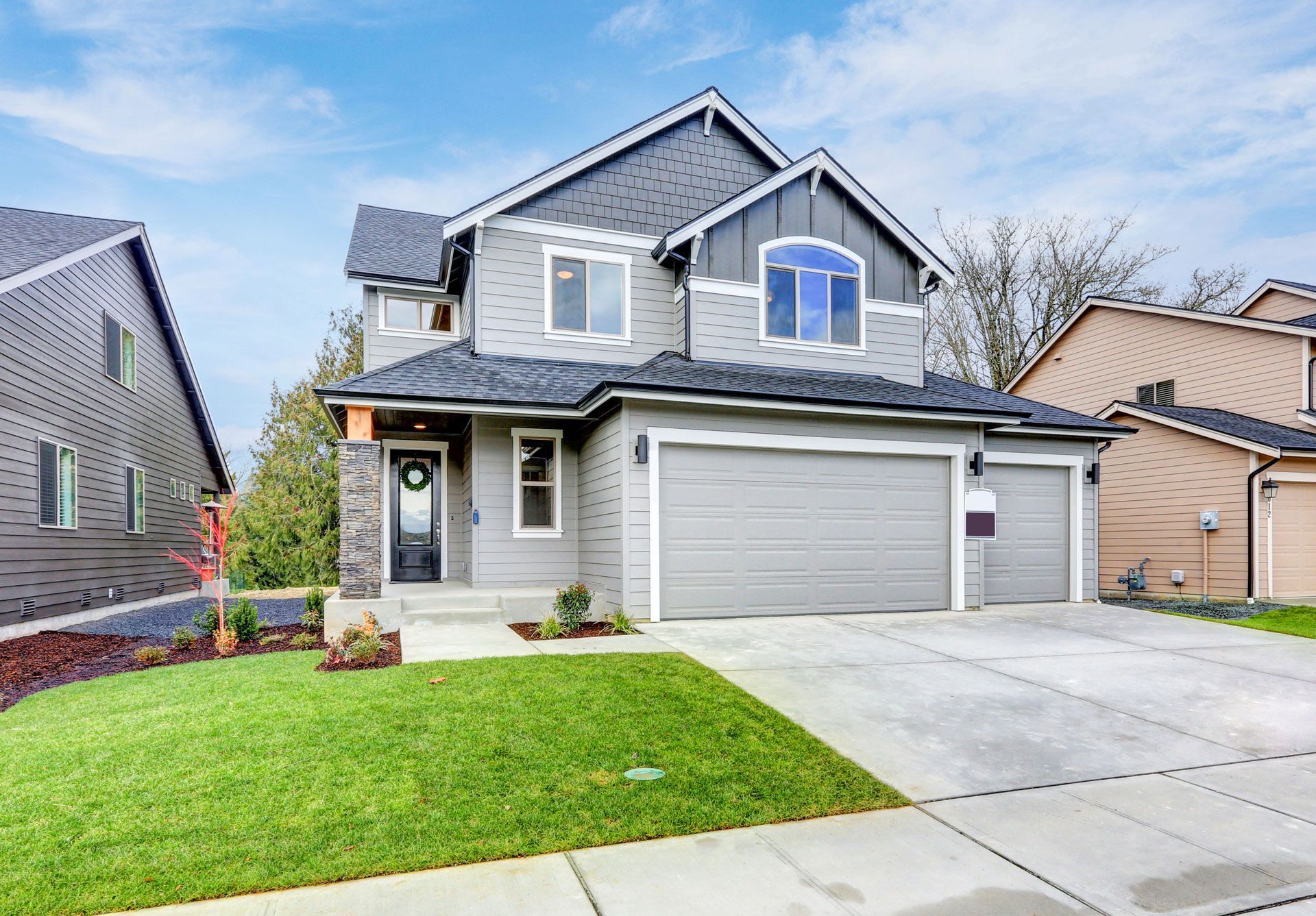 Gray two-story house with a two-car garage, green lawn, and blue sky.