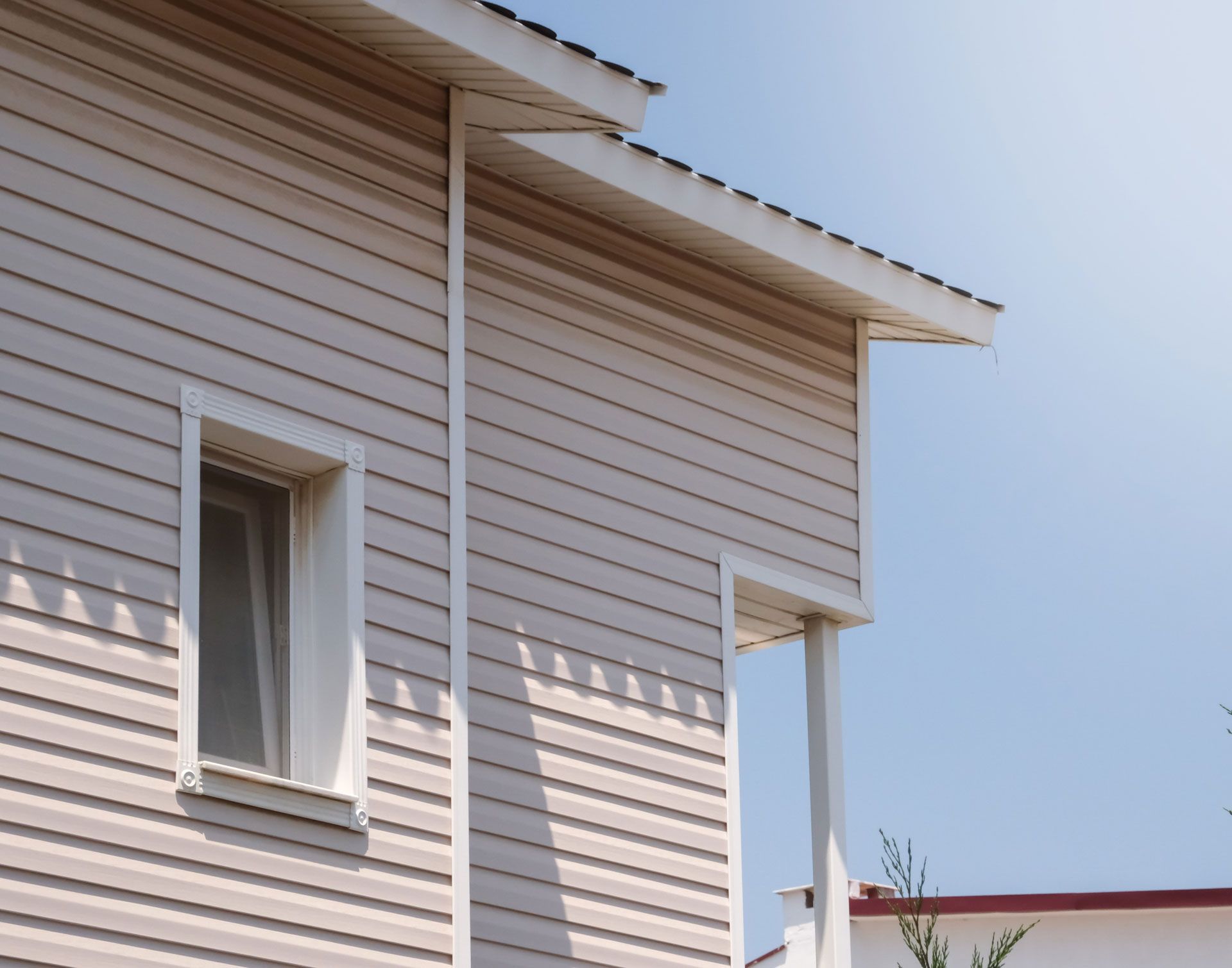 Beige siding of a house with a window, gutter, and porch against a blue sky.