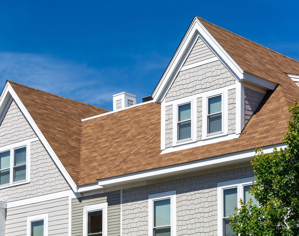 Gray house with brown roof, white trim, blue sky.