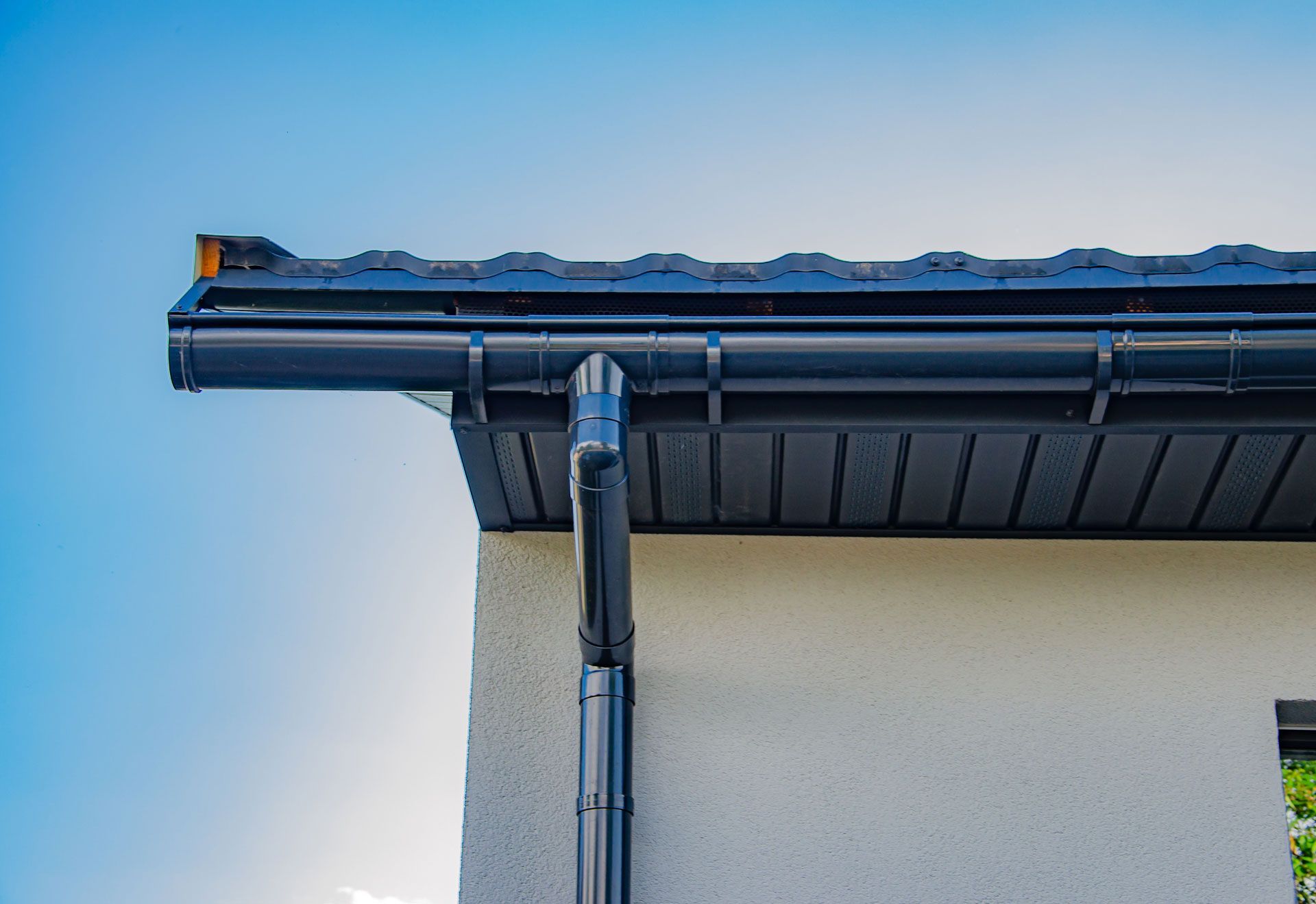 Black gutters on a white building with a dark roof against a bright blue sky.
