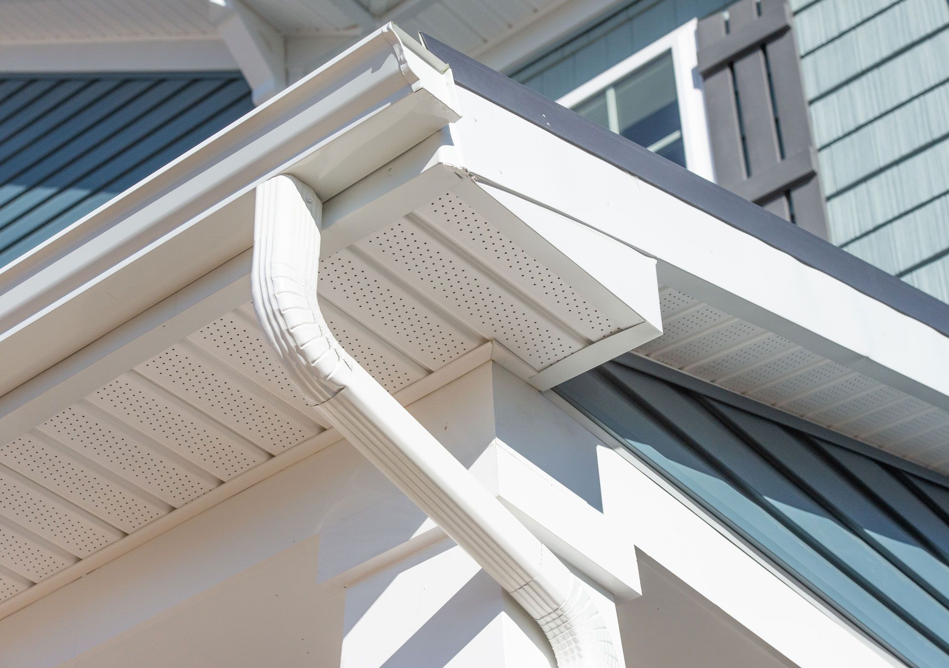 White rain gutter system on a house with light blue siding and dark shutters.