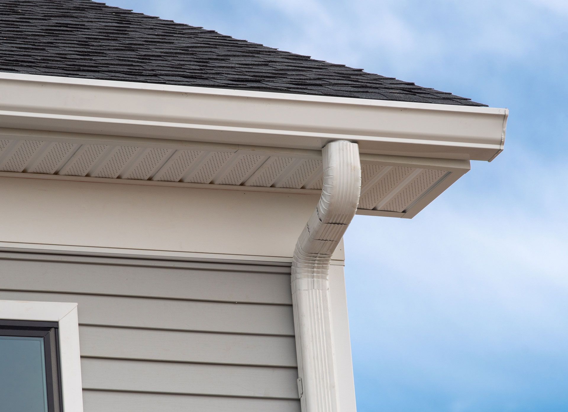 Beige gutters and siding on a house, against a blue sky.
