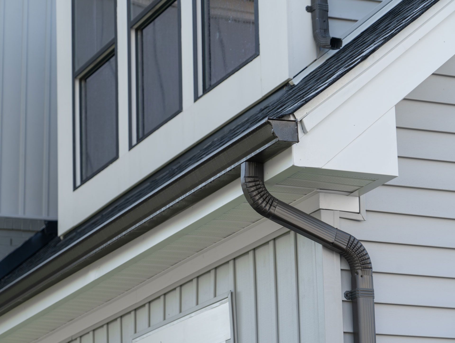 Dark gray gutters on a light gray house, under windows.