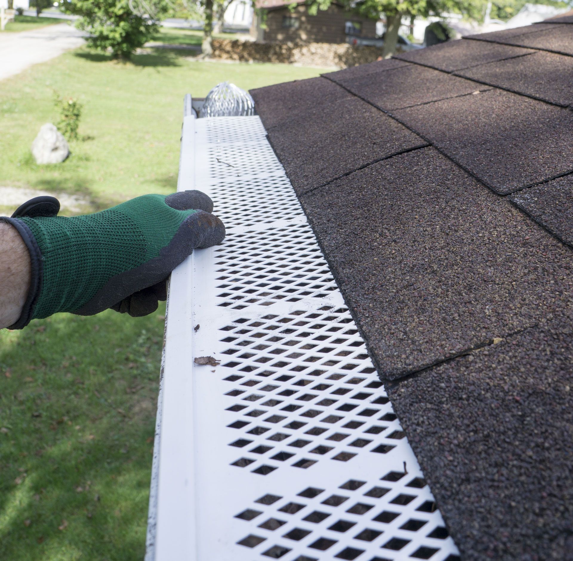 Hand in green glove installing white gutter guard on rooftop.