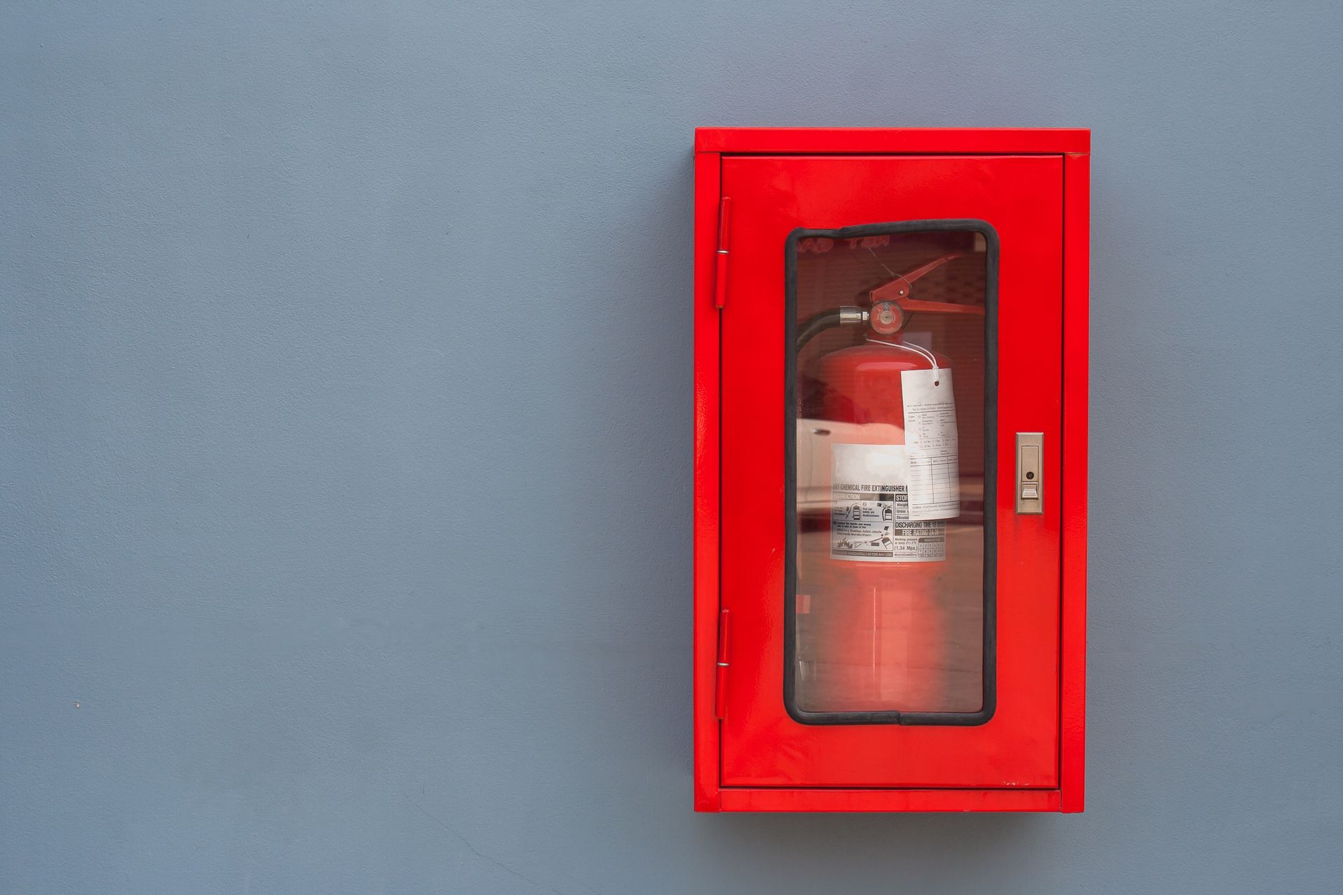 A fire extinguisher is inside a red cabinet, installed on a gray wall.