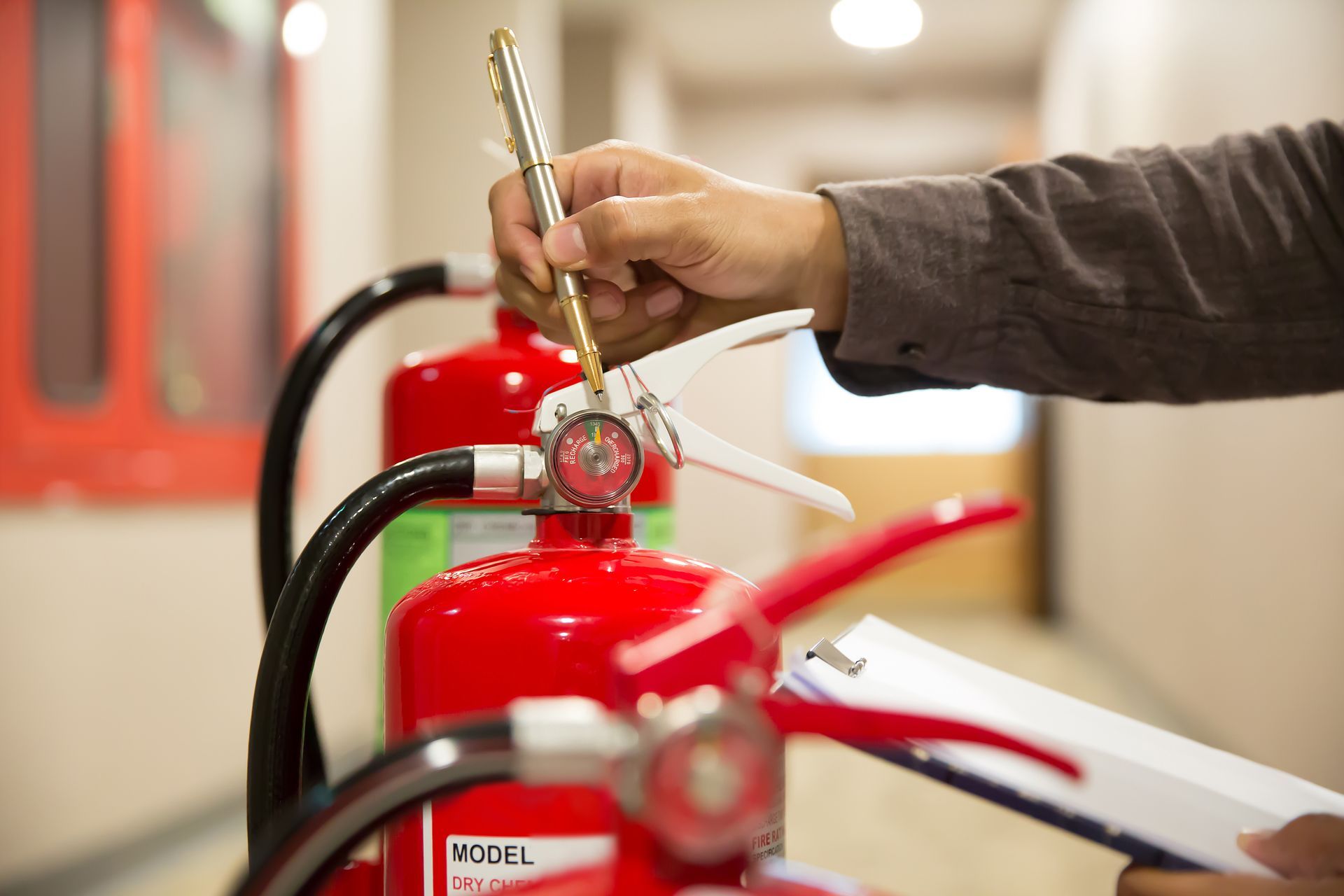 A person inspects a row of red fire extinguishers using a pen while holding a clipboard.
