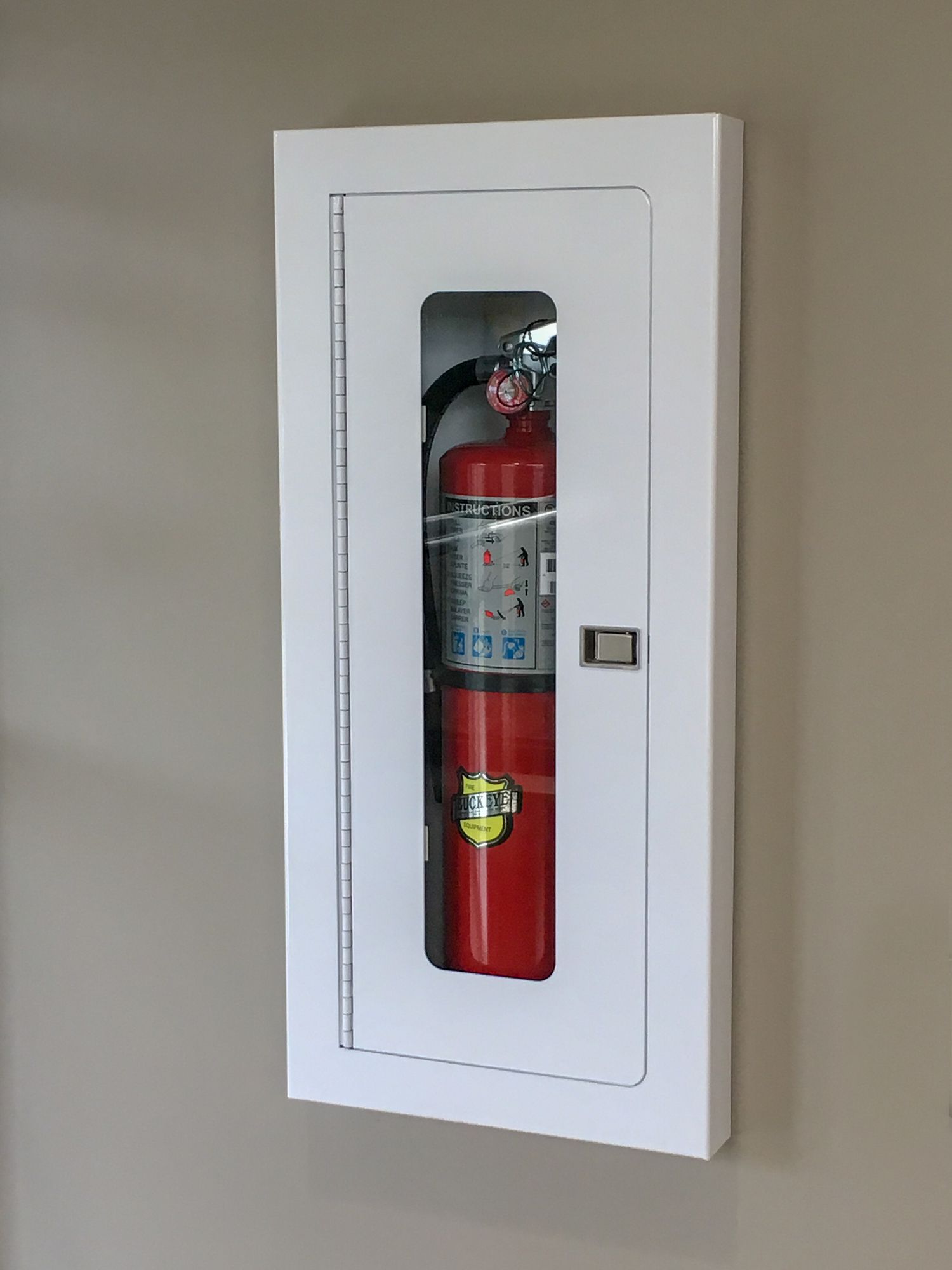 Red fire extinguisher in white cabinet mounted on wall in business office hallway.