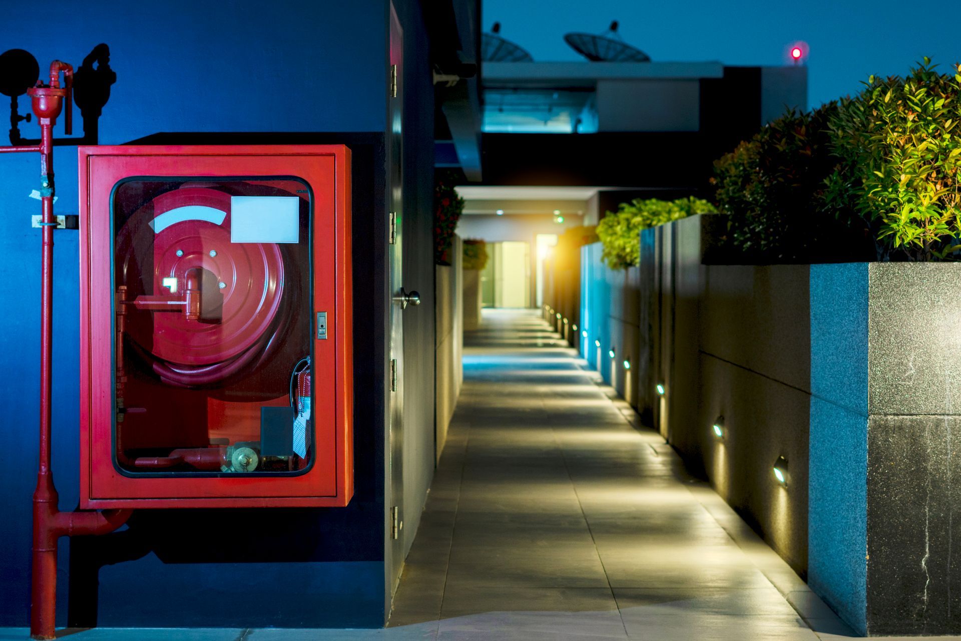 Red fire hose cabinet on wall beside a well-lit walkway at night. Red fire hose cabinet on wall beside a well-lit walkway at night.