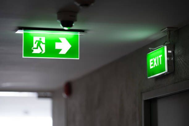 A green exit sign is hanging from the ceiling in a hallway.
