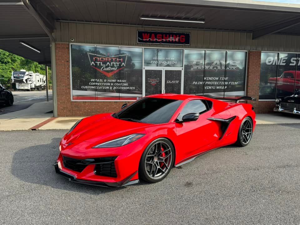 A red sports car is parked in front of a car dealership.