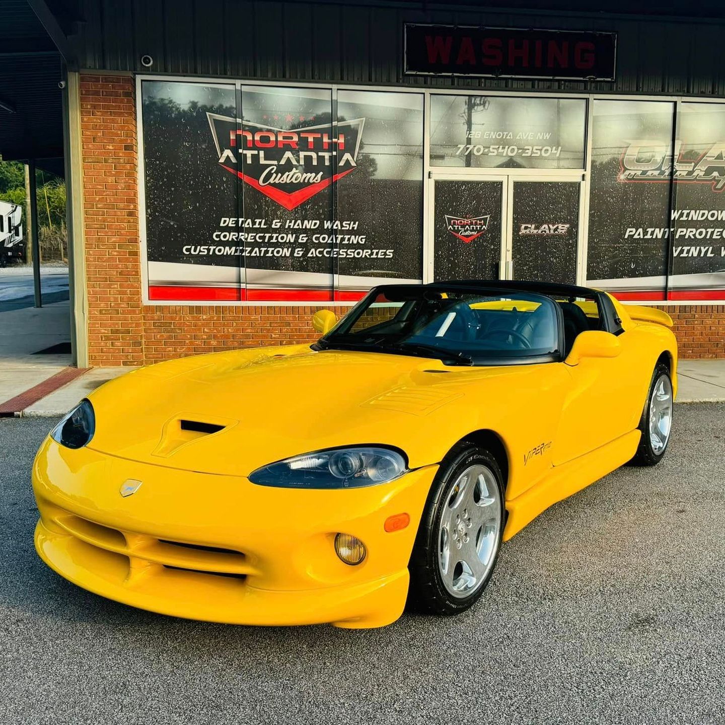 A yellow dodge viper is parked in front of a car dealership.